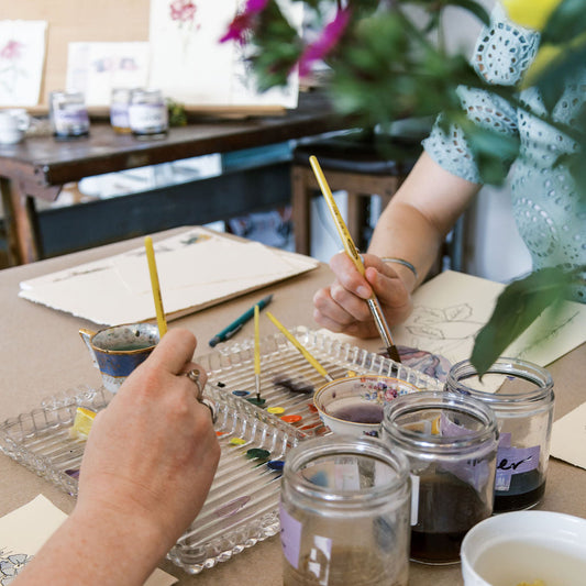 watercolor painting workshop with Marcy Ellis and jars of paint and brushes on a table.