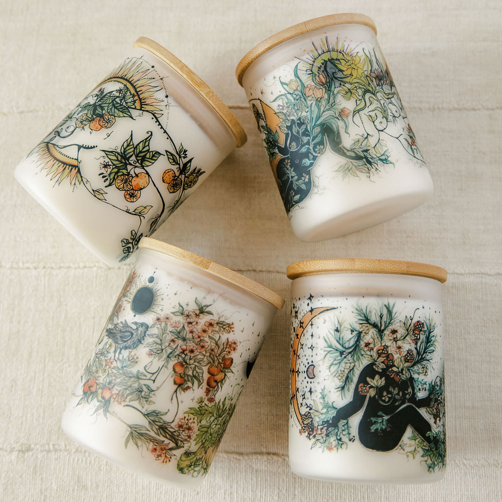 a set of seasonal candles by marcy ellis with seasonal artwork wrapped around a frosted jar with bamboo lid.