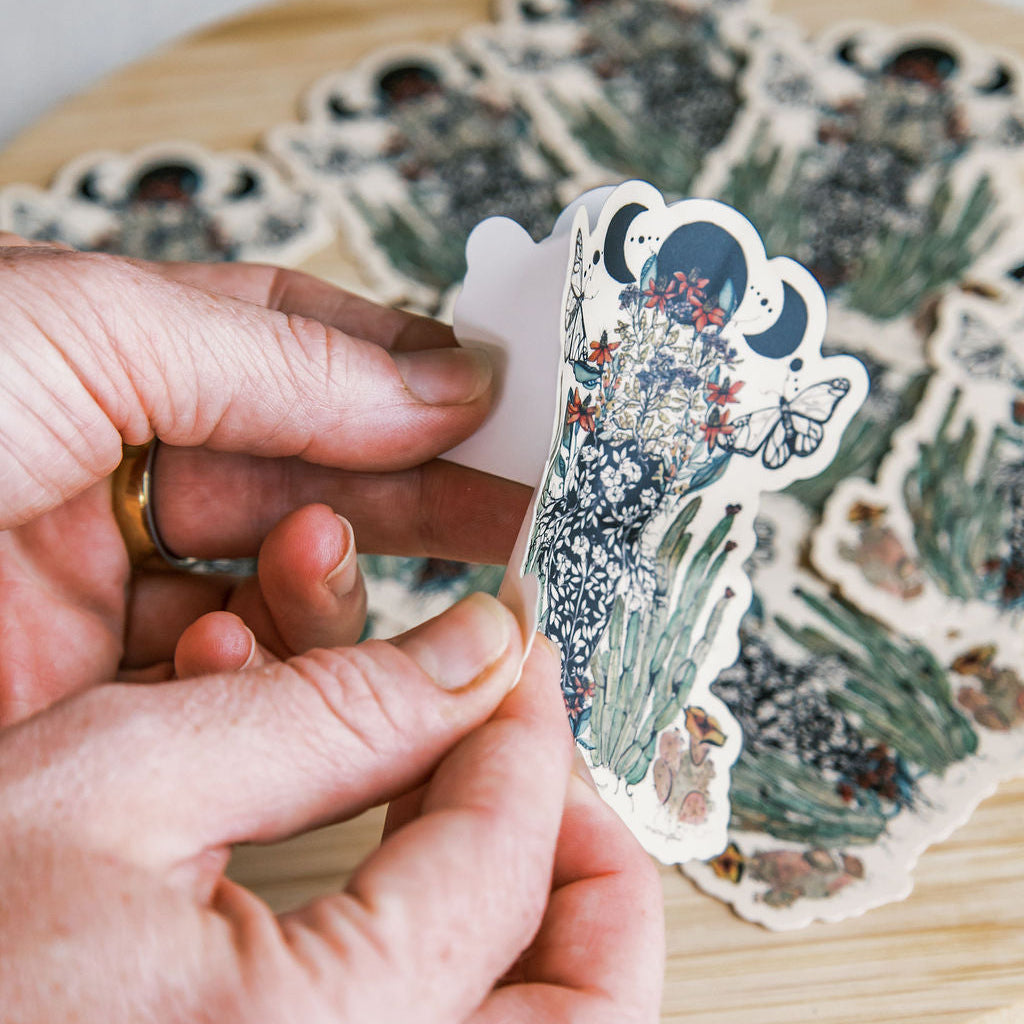 hand-painted watercolor sticker of a feminine figure blooming with desert cacti and a lunar phase. waterproof matte vinyl, designed by tucson artist marcy ellis. a gift for your sister in spirit.