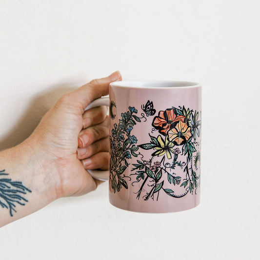 hand holding a Marcy Ellis purple ceramic mug with plant bodies and butterfly 