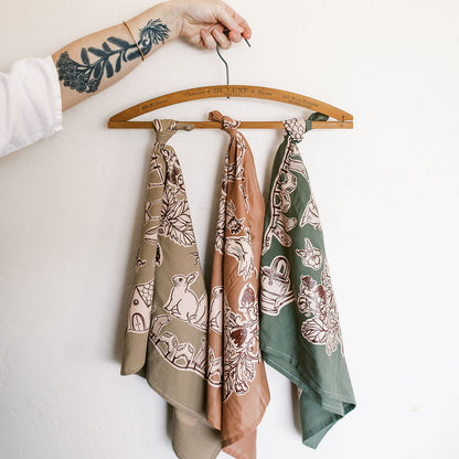 Three patterned scarves hanging on a wooden hanger against a white background