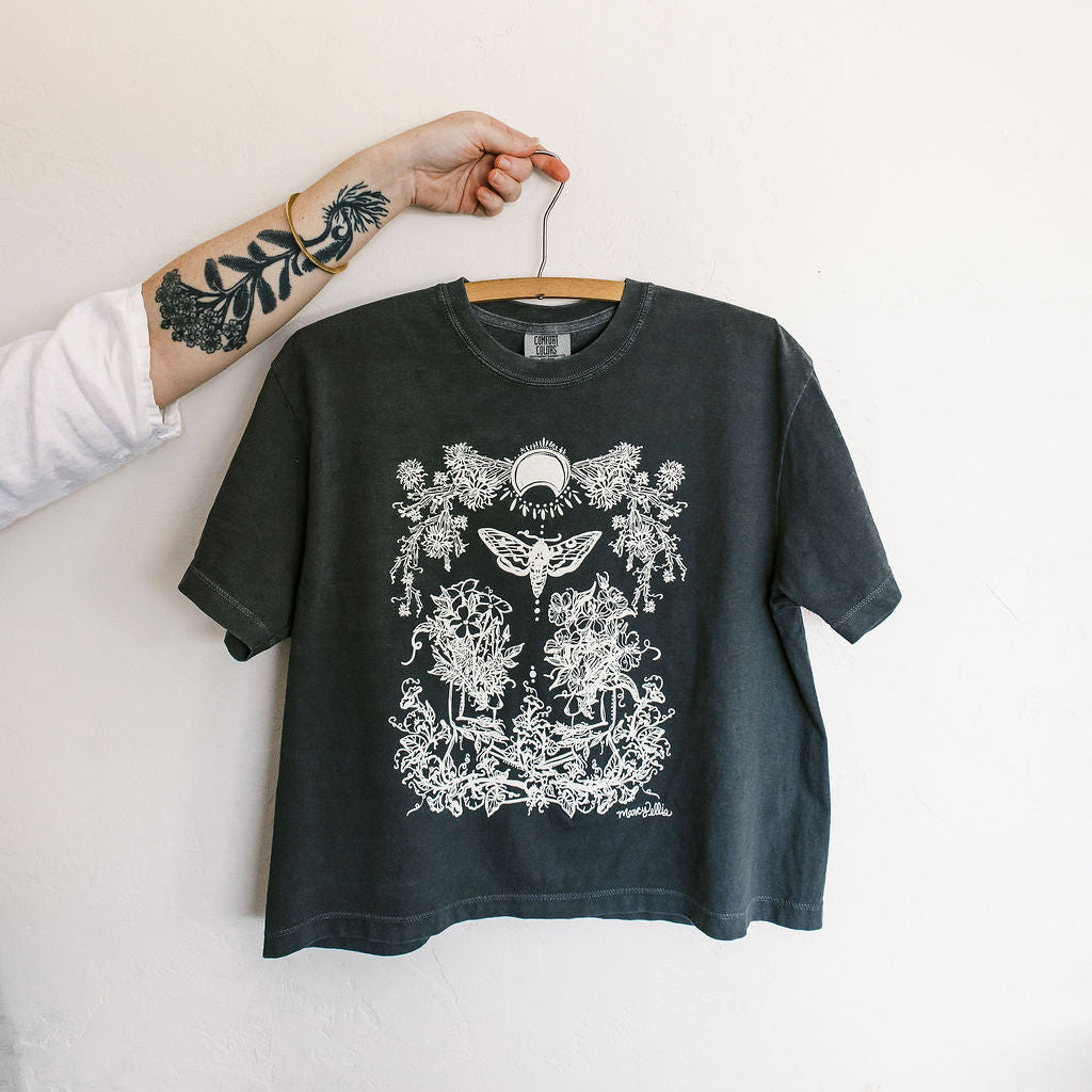 Black t-shirt with white graphic design on a hanger against a plain background