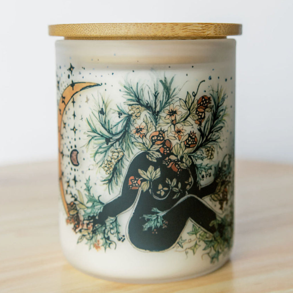 bamboo lid on yule winter solstice soy candle with botanical artwork wrapped around frosted glass jar