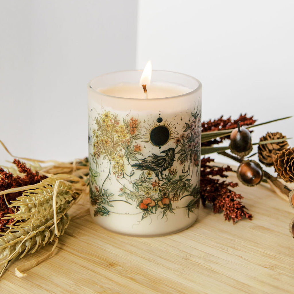 lit mabon fall equinox soy candle with botanical artwork wrapped around frosted glass jar
