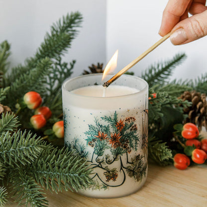 lighting yule winter solstice soy candle with botanical artwork wrapped around frosted glass jar