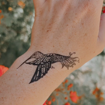 a photo of a hand with a vibrant black temporary tattoo of a hummingbird flying. 