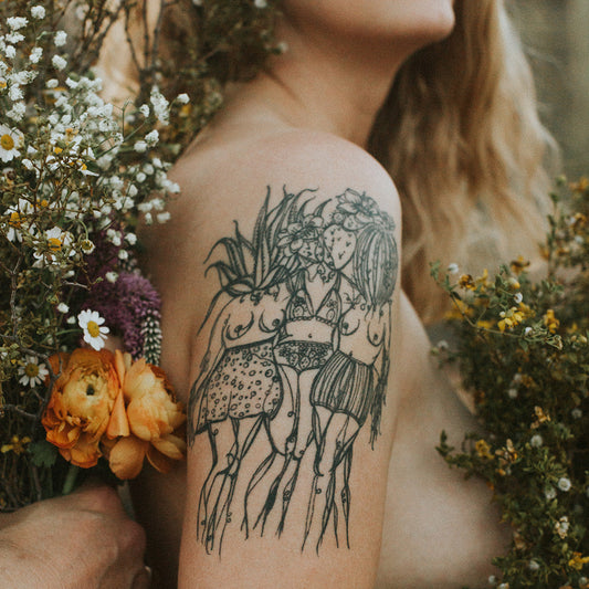 fine line tattoo of three female plant lady botanical figures by marcy ellis on upper arm, framed by dried florals