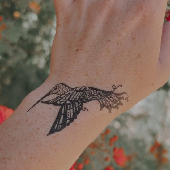 a video of a hand waving, wearing a vibrant, black temporary tattoo of a hummingbird. 